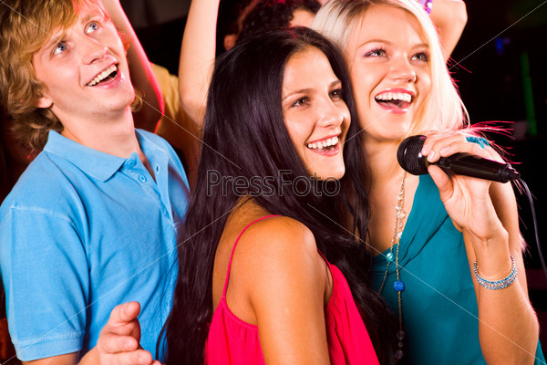 Photo of pretty girls with microphone singing in it and friendly guy behind them