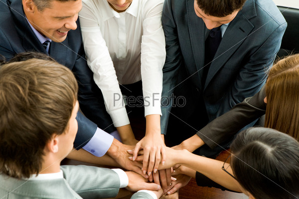 Photo of happy business partners making pile of hands on workplace