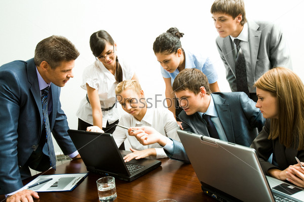 Image of company of successful partners looking at laptop monitor while successful man pointing at it