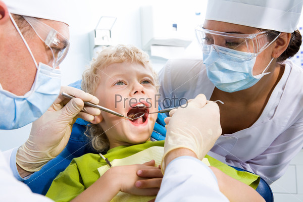 Dental inspection is being given to little boy surrounded by dentist and his assistant