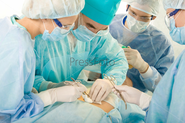 Image of operation: four people in surgical clothes standing near patient