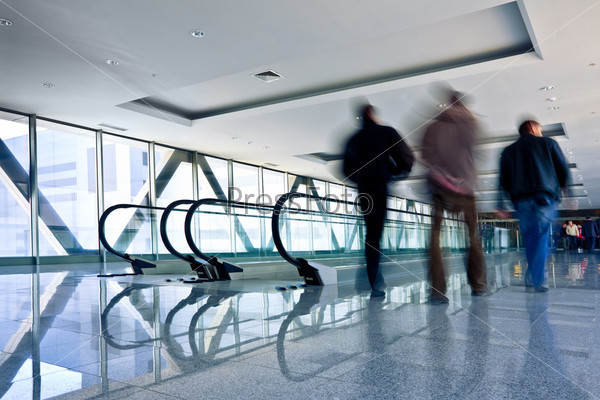 Three men move in grey corridor with escalators in office centre