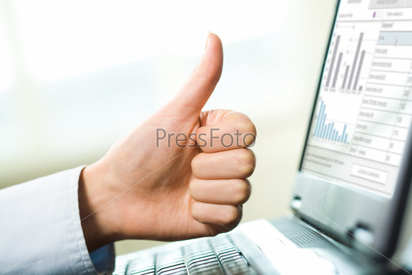 Close-up of female hand keeping thumb up over laptop screen on workplace