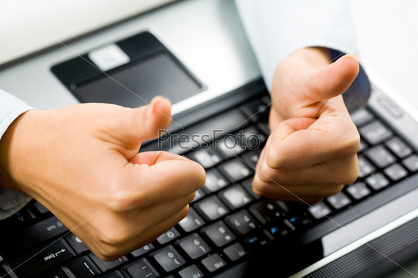 Close-up of female hands with thumbs up over laptop keyboard on workplace