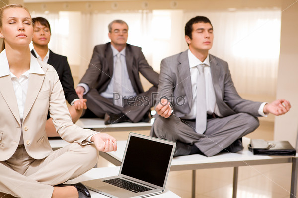 Portrait of meditating business people sitting on desks with their legs crossed in office