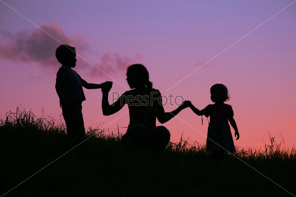 mother holds children for the hands on the sunset