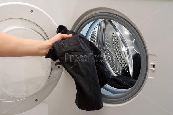 Hand placing the clothes in the drum of washing machine