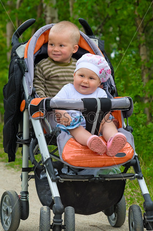 Two children in baby carriage. There is one year\'s difference of age between them. They are brother and sister