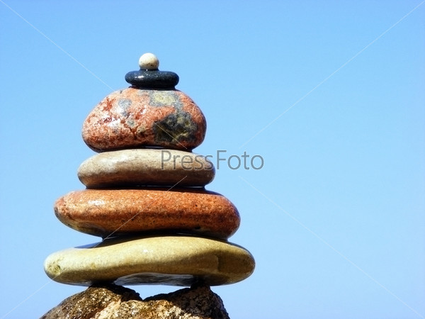 The pyramid of stones on a background of sea and sky with the horizon line in the sun clear cloudless day