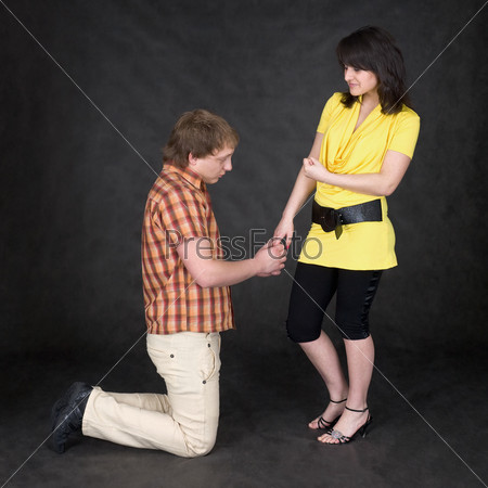 The man is kneeling to the young woman, being sorry