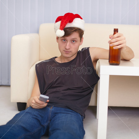 People in christmas hat sits on a floor with beer