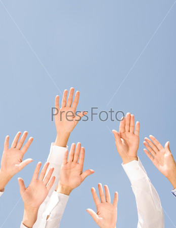 Image of several human palms raised against clear blue sky