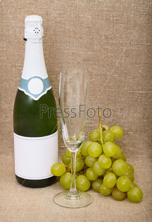 Still-life from a bottle of a sparkling wine, empty glass and grapes against a canvas