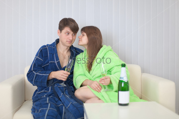 The guy and the girl drink champagne wine on a sofa