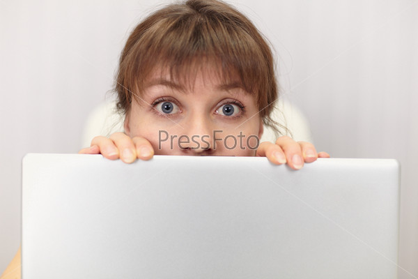 The amusing girl hides behind the laptop screen