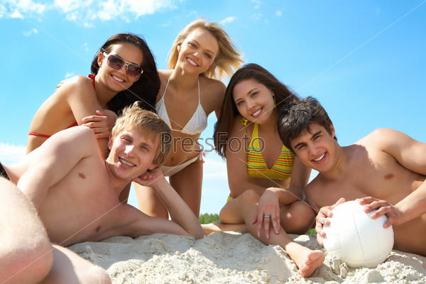 Volleyball team of happy friends sitting on the sand after play
