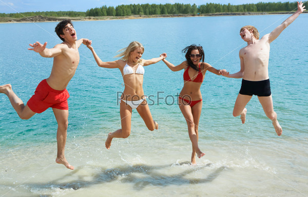 Photo of joyful people holding by hands together and jumping in the lake