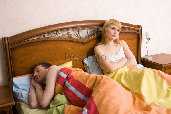 Young couple in a bed bored woman. Woman and man having a disagreement. Male is sleeping and female with sad expressions.