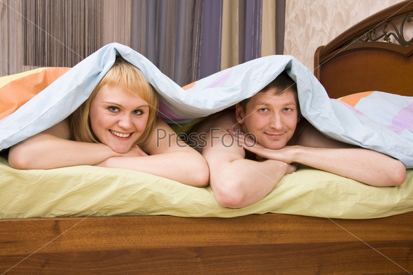 Young attractive happy amorous couple at bedroom. Woman and man are lying on bed. Loving female and male playing in the bed.