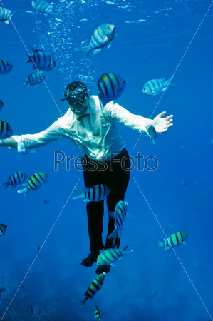 underwater man in a business suit , surrounded by shiny striped fish