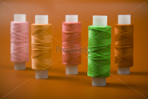 Upright colored spools of thread on a red background