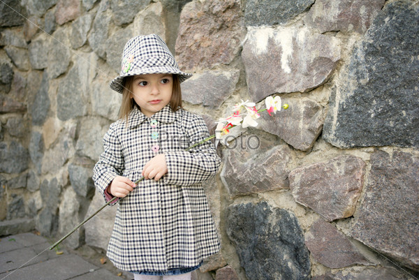 Happy small girl wearing coat, hat and boots, holding white flower an orchid, smiling