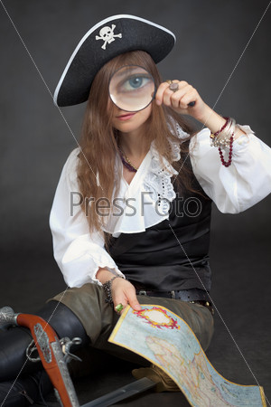 The woman in clothes of the pirate with a sea map and a magnifier glass