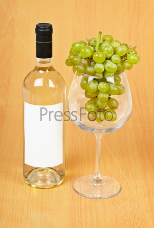 A bottle of wine, a large glass and grapes on wooden background
