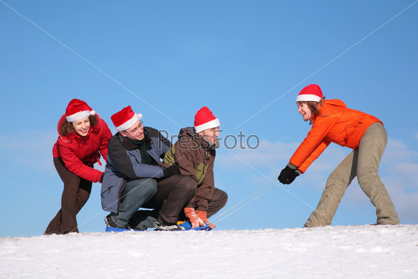 one woman pull two men on sled, other woman push them