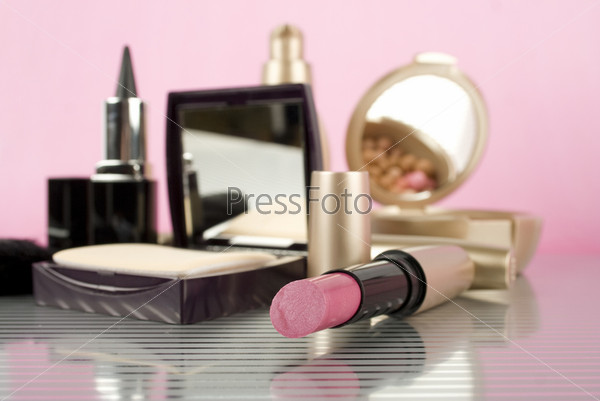 Cosmetics on the table. Basic colors pink and gold. Powder, skin cream, lipstick, handbag, vanity case, brush, eyeliner
