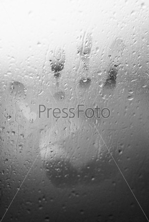 Water drops on glass window with a human hand shape imprinted