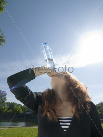 Beautiful red haired girl with bottle of cold water and sun right into the camera