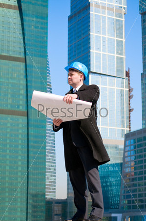 Engineer with blue hard hat holding drawing on skyscrapers background