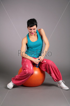 young woman in sportswear sits on orange ball