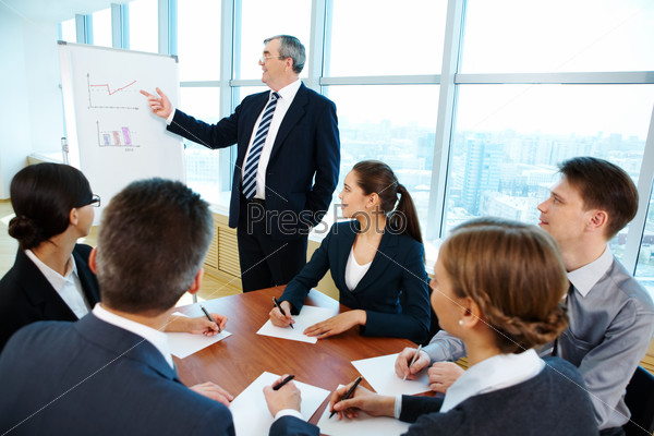 Smart and confident boss pointing at whiteboard while making presentation