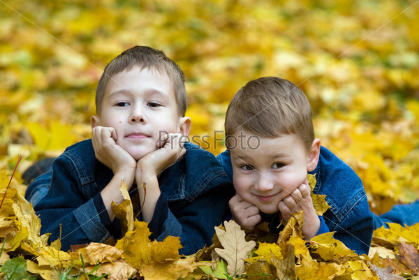 Two boys lay in the fallen autumn foliage