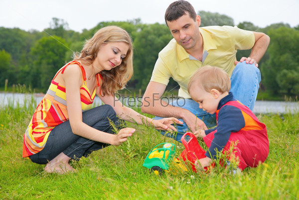 child sits on grass with parents and plays with toy
