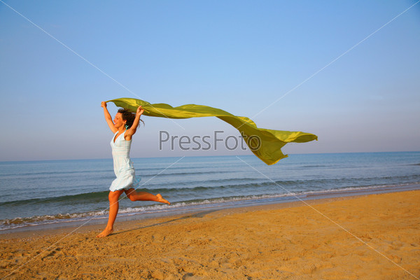 Young girl runs on edge of sea with yellow fabric shawl in hands