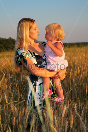 Mother holds child on hands in wheaten field