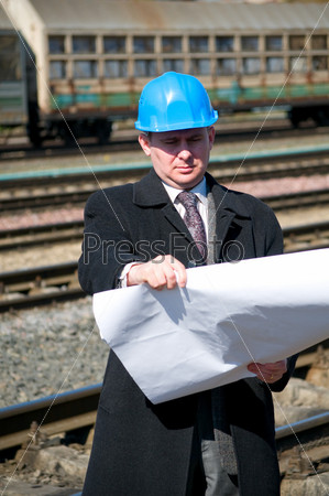 Engineer with white hard hat holding drawing near train