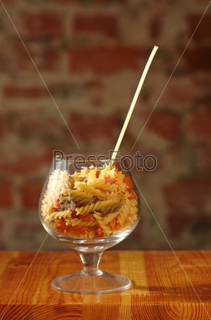 Macaroni in cognac glass with straw from spaghetti on brick wall background