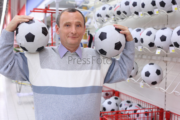 elderly man in shop with footballs in hands