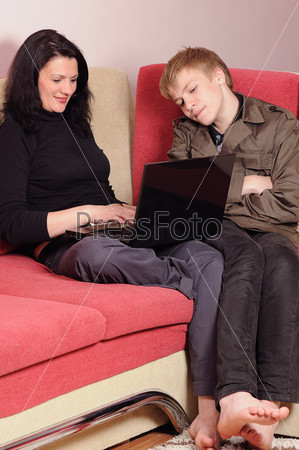 Mother and the son with a laptop sit on a sofa