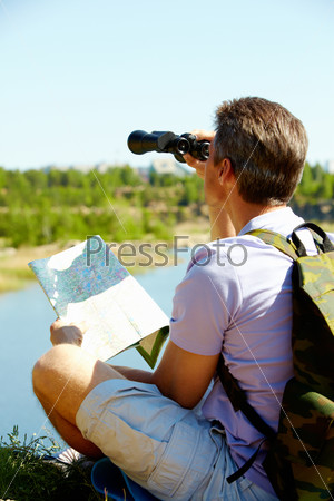 Back view of male tourist looking through binoculars in the country