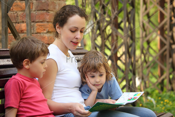 Mother reads book for children sits on bench