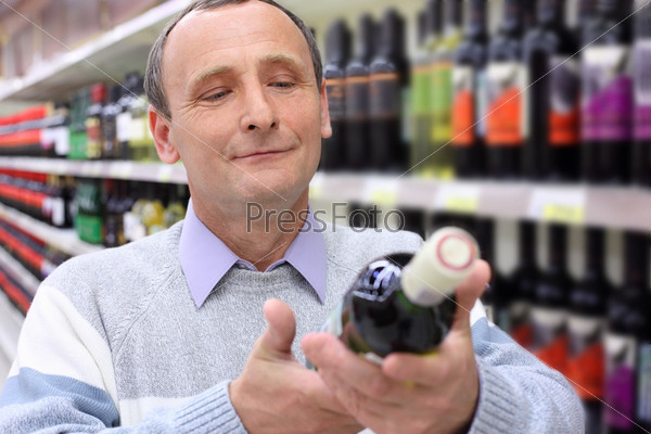 happy elderly man in shop looks on  wine bottle in hands