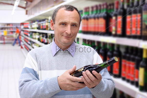 elderly man in shop with wine bottle in hands