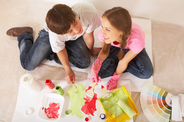 Above angle of young couple mixing paints while sitting on floor in new flat