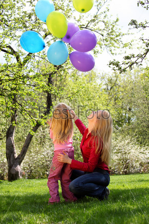 Mother with daughter with sheaf of balloons in garden in spring