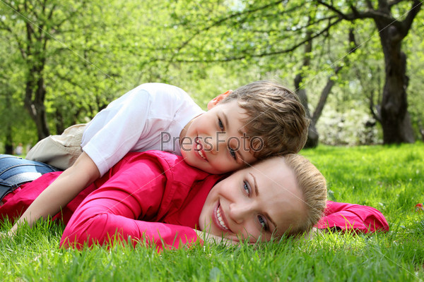 son lies on back of mother lying on grass in park in spring